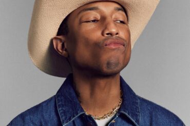 pharrell williams wearing a cowboy hat, denim jacket and yellow gold tiffany and co necklace while pouting